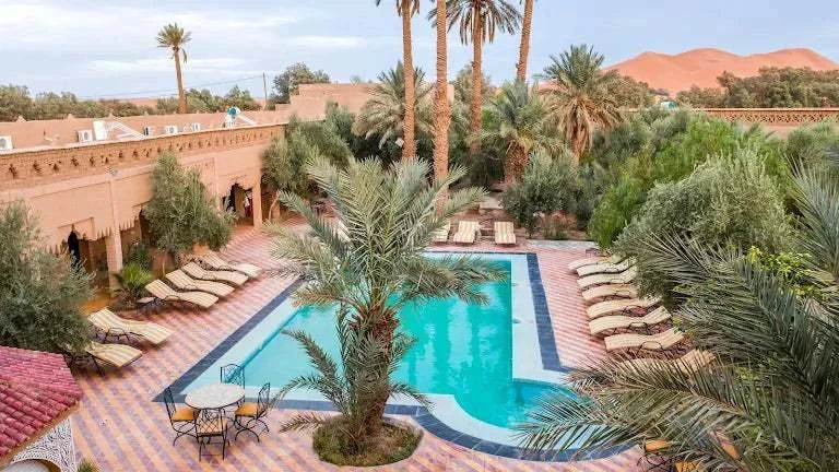 Kasbah Le Touareg outdoor swimming pool surrounded by palm trees, terracotta walls, and sun loungers in Merzouga Morocco