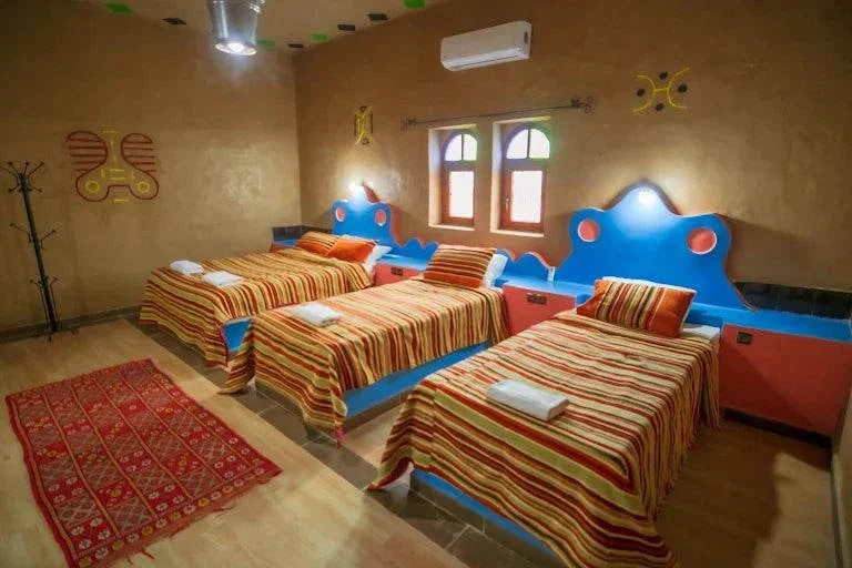 Kasbah Le Touareg traditional bedroom with three twin beds featuring blue headboards and red striped blankets in a warm-toned room