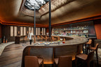 Bar area with curved wooden bar counter, brown leather chairs, warm lighting, and decorative lattice ceiling detail at La Mamounia Marrakech
