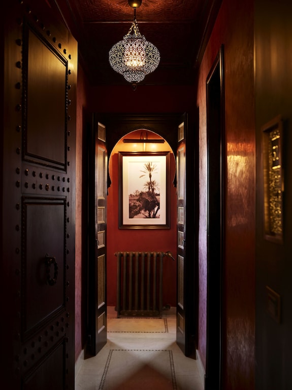 La Mamounia Marrakech narrow corridor with dark wooden doors, patterned tiled floor, decorative arched doorway, and intricate hanging lantern
