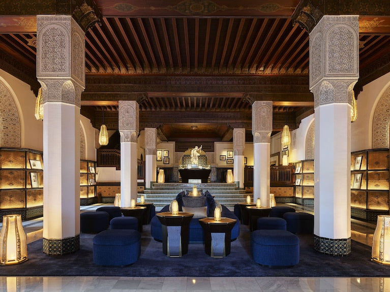 Elegant lounge area in La Mamounia Marrakech with navy blue velvet seating, ornate pillars, wooden ceiling, and warm lighting