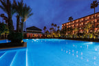La Mamounia Marrakech outdoor illuminated swimming pool surrounded by palm trees and luxurious hotel building at dusk