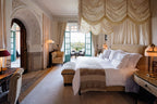 Luxury hotel bedroom at La Mamounia Marrakech featuring elegant beige and gold tones, ornate Moroccan archways, and a canopy bed with crisp white linens.