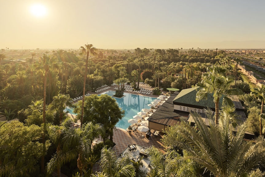 La Mamounia Marrakech luxury hotel with large blue swimming pool, white sun loungers, and lush green palm trees under warm sunlight