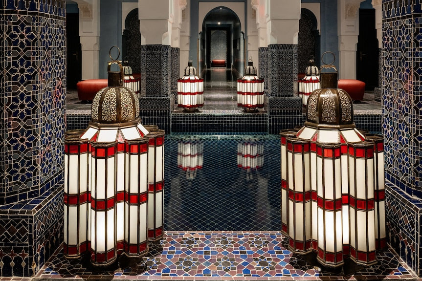 La Mamounia Marrakech Moroccan lanterns with red and white glass panels surrounding a reflective dark blue tiled pool and intricate mosaic columns