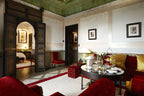 Luxurious Moroccan-style sitting room at La Mamounia Marrakech featuring ornate wooden doors, red velvet chairs, and a round table with refreshments