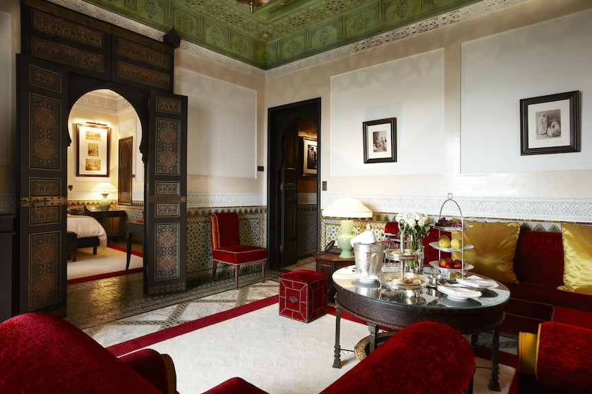 Luxurious Moroccan-style sitting room at La Mamounia Marrakech featuring ornate wooden doors, red velvet chairs, and a round table with refreshments