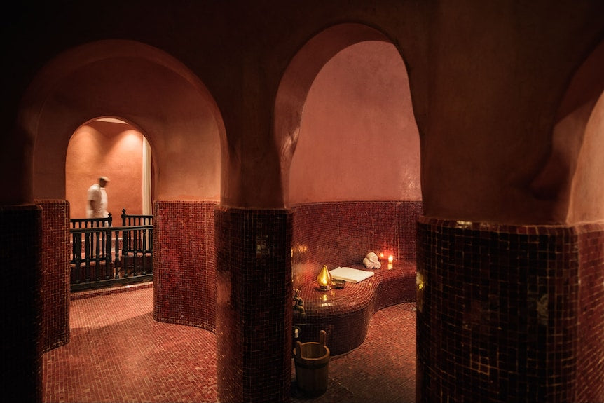 La Mamounia Marrakech spa interior with warm terracotta walls, red mosaic tiles, arched doorways, and ambient lighting