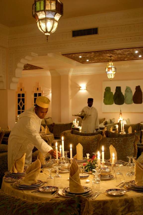 Le Berbere Palace Ouarzazate elegant dining room with traditional decor, candlelit table setting and staff in classic attire