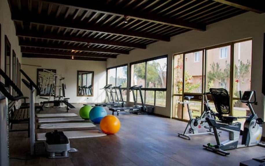 Le Berbere Palace Ouarzazate gym room with wooden ceiling, large windows, treadmills, recumbent bikes, and colorful exercise balls