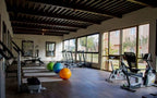 Le Berbere Palace Ouarzazate gym room with wooden ceiling, large windows, treadmills, recumbent bikes, and colorful exercise balls
