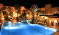 Le Berbere Palace Ouarzazate illuminated outdoor swimming pool with palm trees and lounge chairs at night
