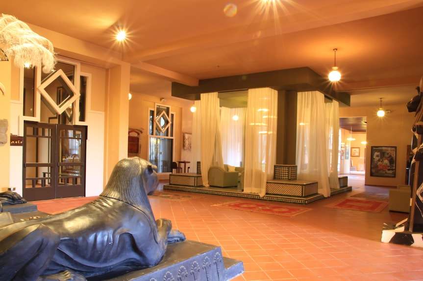 Le Berbere Palace Ouarzazate hotel lobby with orange tiled floor, bronze lion statue, lounge area enclosed by sheer curtains and warm lighting