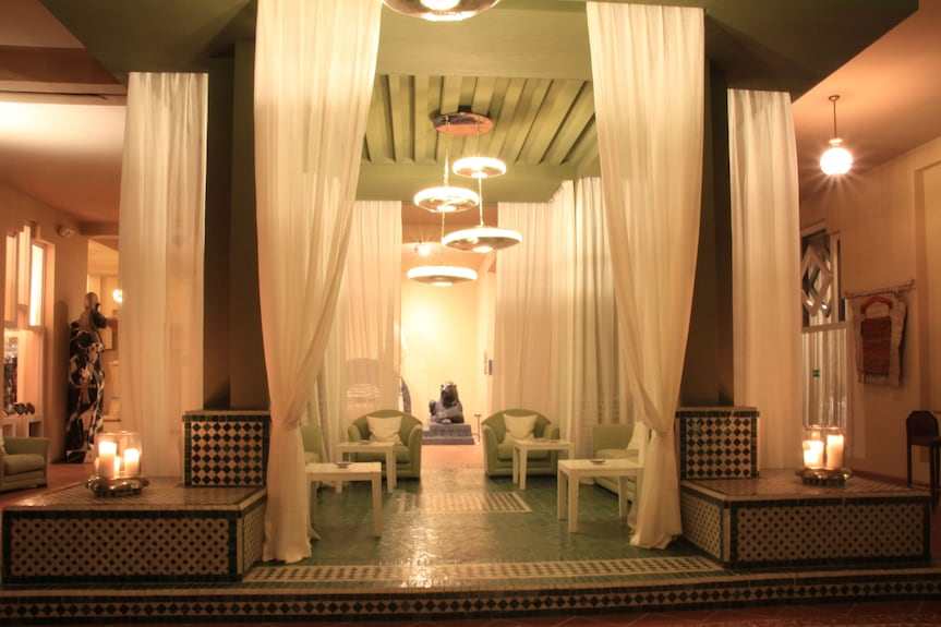 Le Berbere Palace Ouarzazate hotel lounge with olive green tiled floors, cream sheer curtains, and cozy seating area