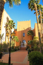 Le Berbere Palace Ouarzazate luxury hotel in Morocco with peach-colored towers, lush palm trees, and decorative entrance pathway