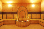 Le Berbere Palace Ouarzazate spa room with warm orange marble walls, traditional Moroccan tile accents, and a central wooden platform with towels and candles