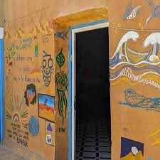 Le Gout Du Sahara Hostel wall mural with colorful desert-themed designs and an open blue door on textured yellow-orange surface