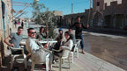 Outdoor white plastic chairs and tables with six people sitting and smiling in casual attire at Le Gout Du Sahara Hostel.