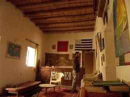 Le Gout Du Sahara Hostel interior with wooden ceiling, rustic decor, Moroccan rugs, and a person standing by the window.