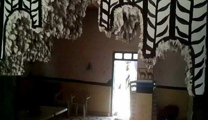 Interior of Le Gout Du Sahara Hostel featuring dark walls with white tribal decorative patterns and a doorway with light streaming in.