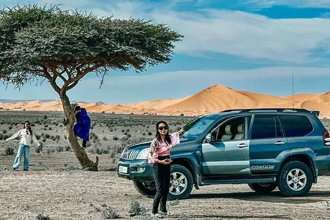 Desert scene with a black and grey SUV parked near a tree and golden sand dunes in the background at Les Pyramides Hotel.