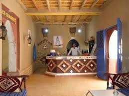 Hotel reception area featuring a decorative wooden counter with geometric patterns, beige walls, and traditional Moroccan decor at Les Pyramides Hotel.