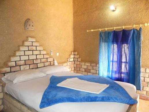 Hotel room with beige textured walls and brick accents, featuring a double bed with blue blanket and white towel, highlighting Les Pyramides Hotel.