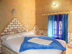 Hotel room with beige textured walls and brick accents, featuring a double bed with blue blanket and white towel, highlighting Les Pyramides Hotel.