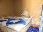 Hotel room with beige brick walls, blue carpet, white bedding, and blue towels folded in a star shape at Les Pyramides Hotel.