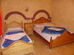 Twin bedroom with two wooden framed beds, beige walls, blue and white bed linens, and a central wooden nightstand at Les Pyramides Hotel.