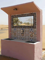 Outdoor pink concrete water sink with colorful geometric mosaic tile backsplash and a rectangular mirror at Les Pyramides Merzouga desert campsite.