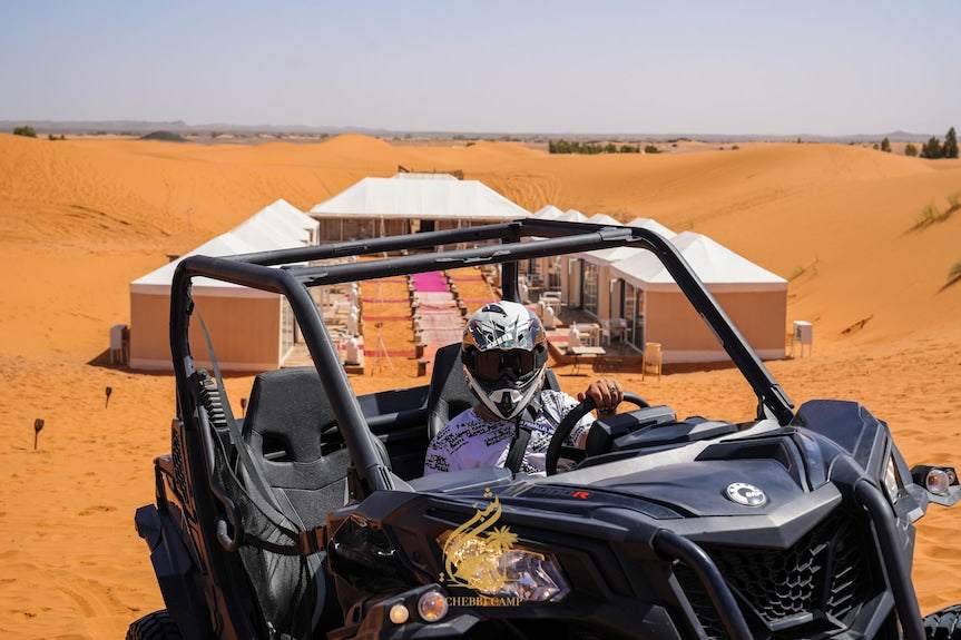 Luxury Camp Chebbi off-road black dune buggy vehicle with driver in helmet on desert sand with white tents in background