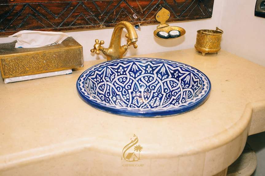 Luxury Camp Chebbi blue and white ceramic sink with intricate floral patterns and a vintage brass faucet on beige countertop