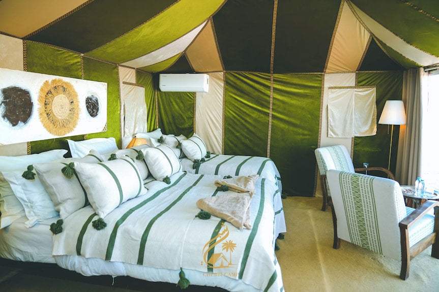 Luxury Camp Chebbi tent room with green and beige fabric walls, twin beds with white and green bedding, and wooden chairs