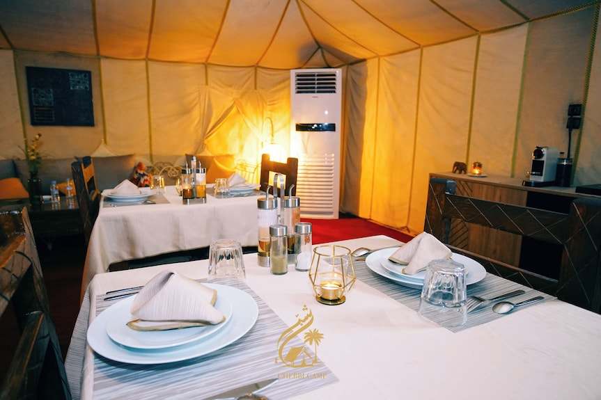 Luxury Camp Chebbi dining area inside a beige tent with neatly set tables including white plates, cloth napkins, and glassware
