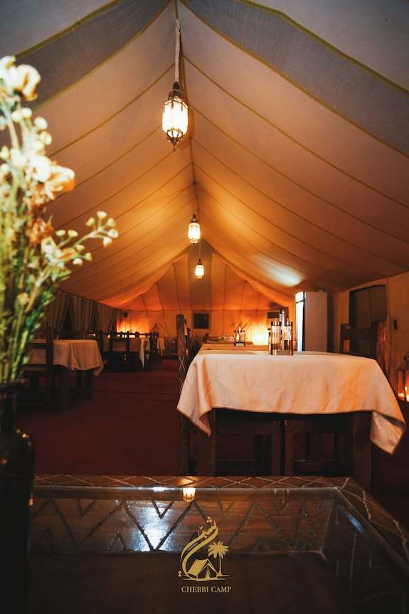 Luxury Camp Chebbi interior with warm lighting, beige fabric ceiling, wooden tables, and cozy dining setup