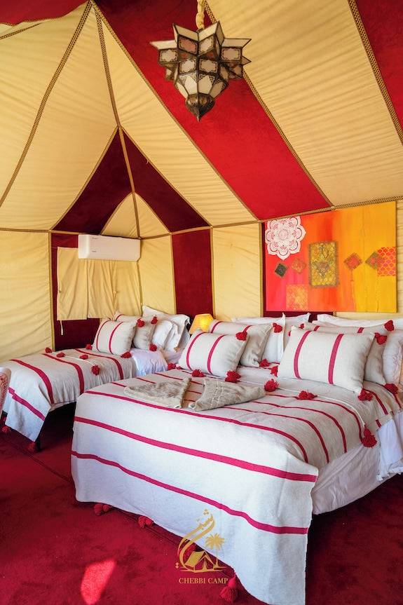 Luxury Camp Chebbi beige and red striped tent interior featuring two beds with matching bedding and decorative cushions