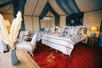Luxury Camp Chebbi tent interior with beige and blue striped fabric walls, double bed with striped bedding, and cozy rustic furniture