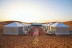 Luxury Camp Chebbi white canvas tents with large windows arranged in two rows on desert sand at sunset