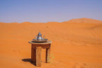 Luxury Camp Chebbi wooden stool with traditional silver teapot on a round tray set on orange desert sand under clear blue sky
