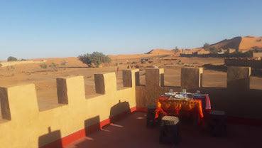 Maison Riad Tamarighte beige adobe terrace with crenellated walls and a table set against Moroccan desert landscape