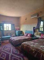 Maison Riad Tamarighte bedroom with twin beds, traditional Moroccan patterned throws, dark wood furniture, windows, and a decorative rug
