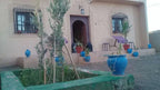 Maison Riad Tamarighte beige exterior with arched wooden doorway, iron window grills, and blue ceramic pots with plants