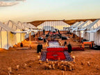 Maison Riad Tamarighte luxury desert camp with white canvas tents, red carpets, lanterns, and seated guests on sandy ground