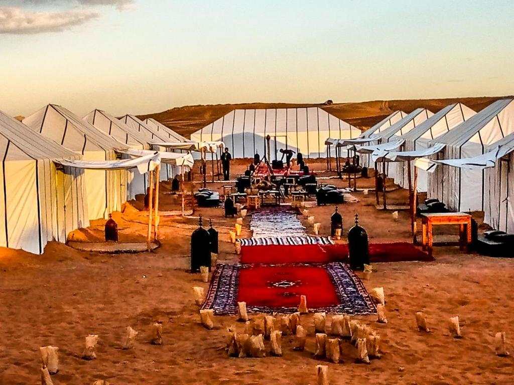 Maison Riad Tamarighte luxury desert camp with white canvas tents, red carpets, lanterns, and seated guests on sandy ground