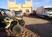 Maison Riad Tamarighte beige sandstone building with traditional Moroccan design, parked white vans and an off-road buggy outside