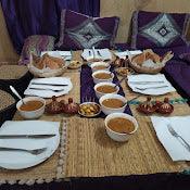 Moroccan dining setup with multiple white plates, ceramic bowls filled with soup, traditional bread, and appetizers on a woven mat, showcasing Maison Riad Tamarighte hospitality