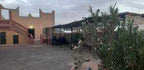 Maison Riad Tamarighte traditional Moroccan riad in soft beige with outdoor courtyard, palm trees, and adobe walls under cloudy sky