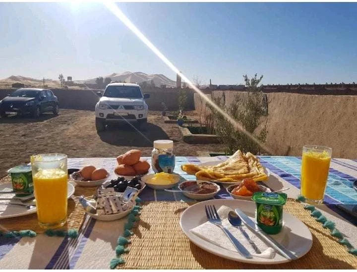 Maison Riad Tamarighte outdoor breakfast setup with glasses of orange juice, eggs, crepes, jam, and yogurt on a colorful tablecloth under sunlight