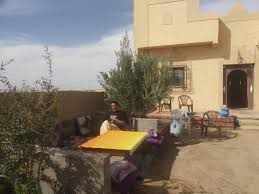 Maison Riad Tamarighte outdoor seating area with yellow table, cushioned benches, and earthen walls in desert setting